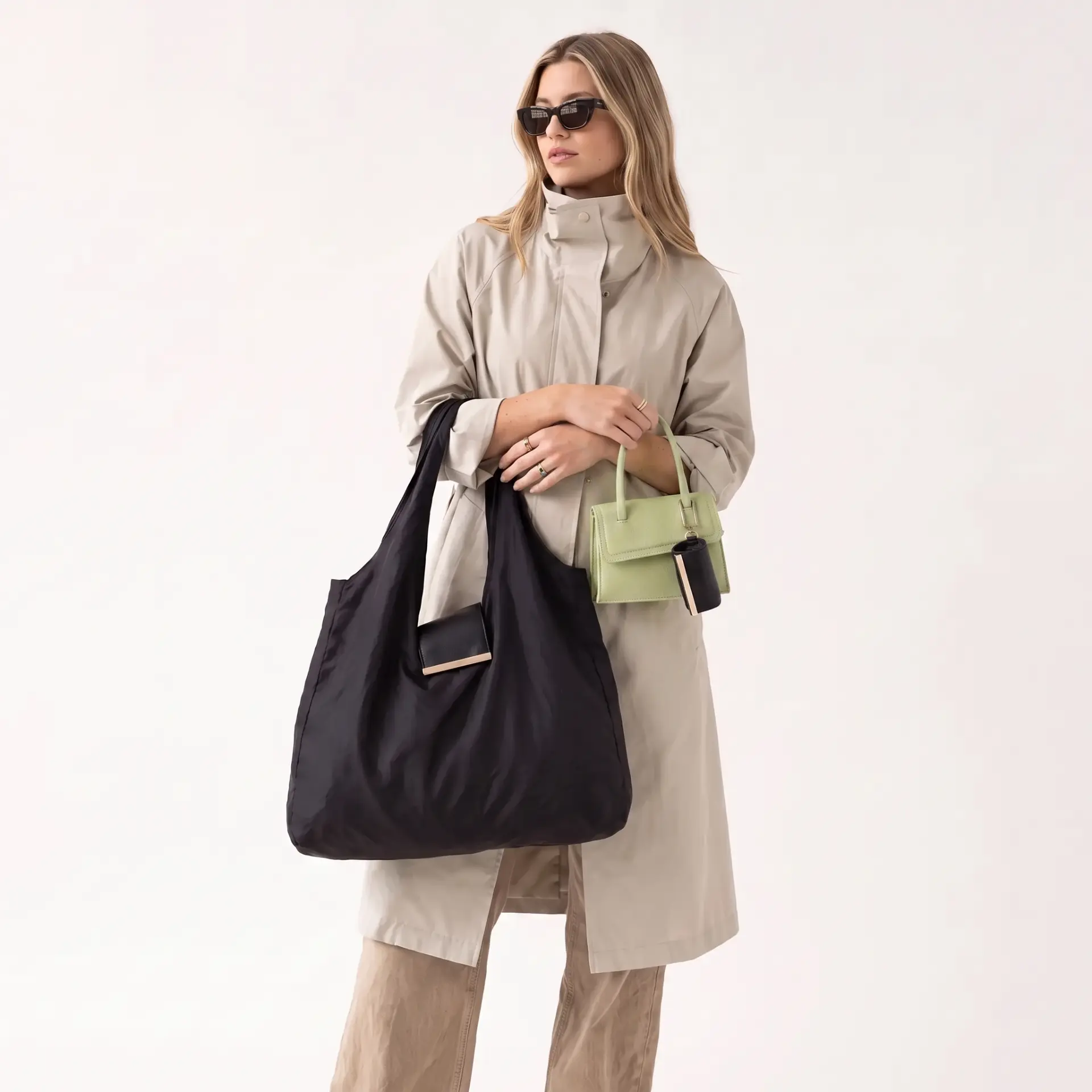 Model in a trench coat holding the black Cliqué Tote and a green mini bag