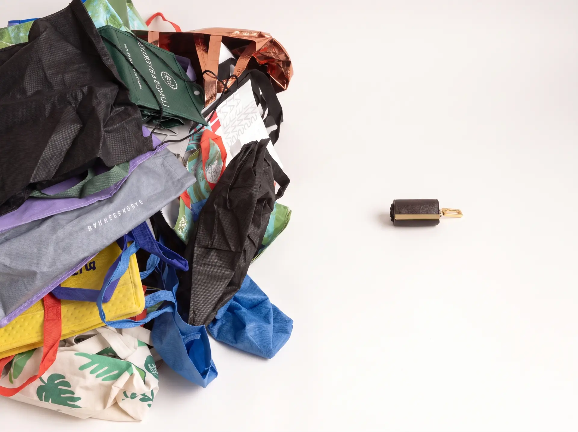 A pile of bulky tote bags beside one small folded cliqué tote pouch