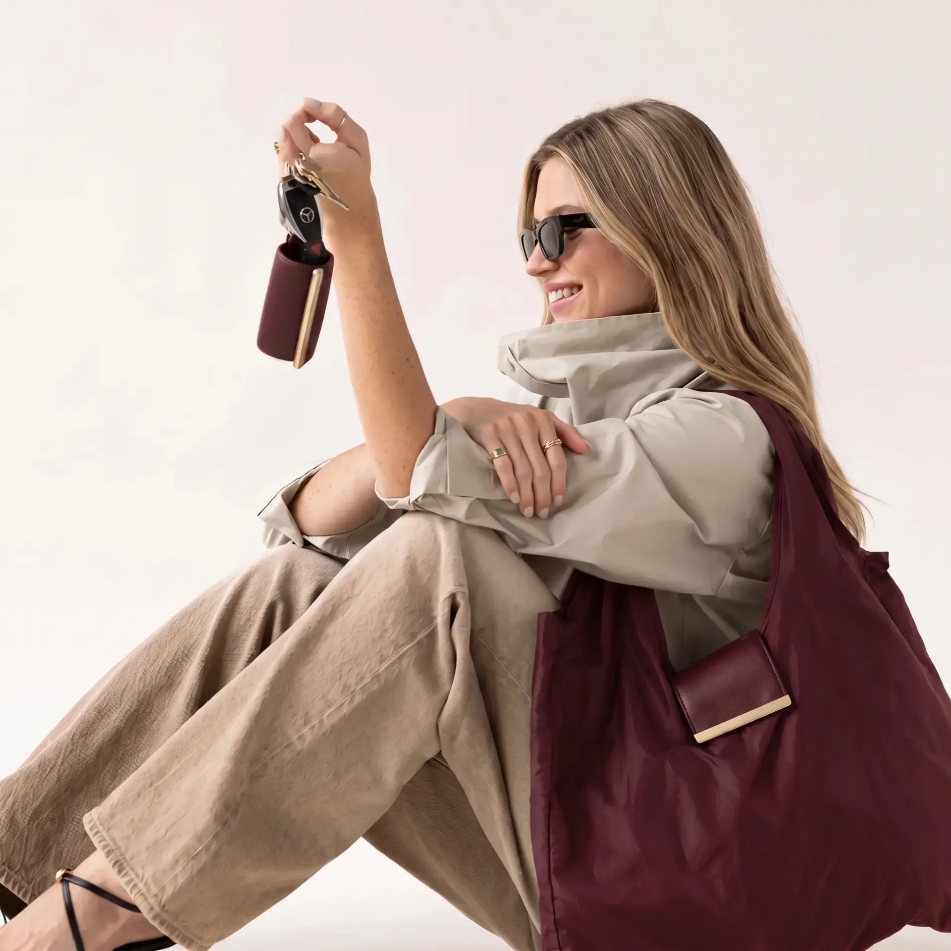 Model seated holding keys with the burgundy Cliqué Tote pouch clipped on
